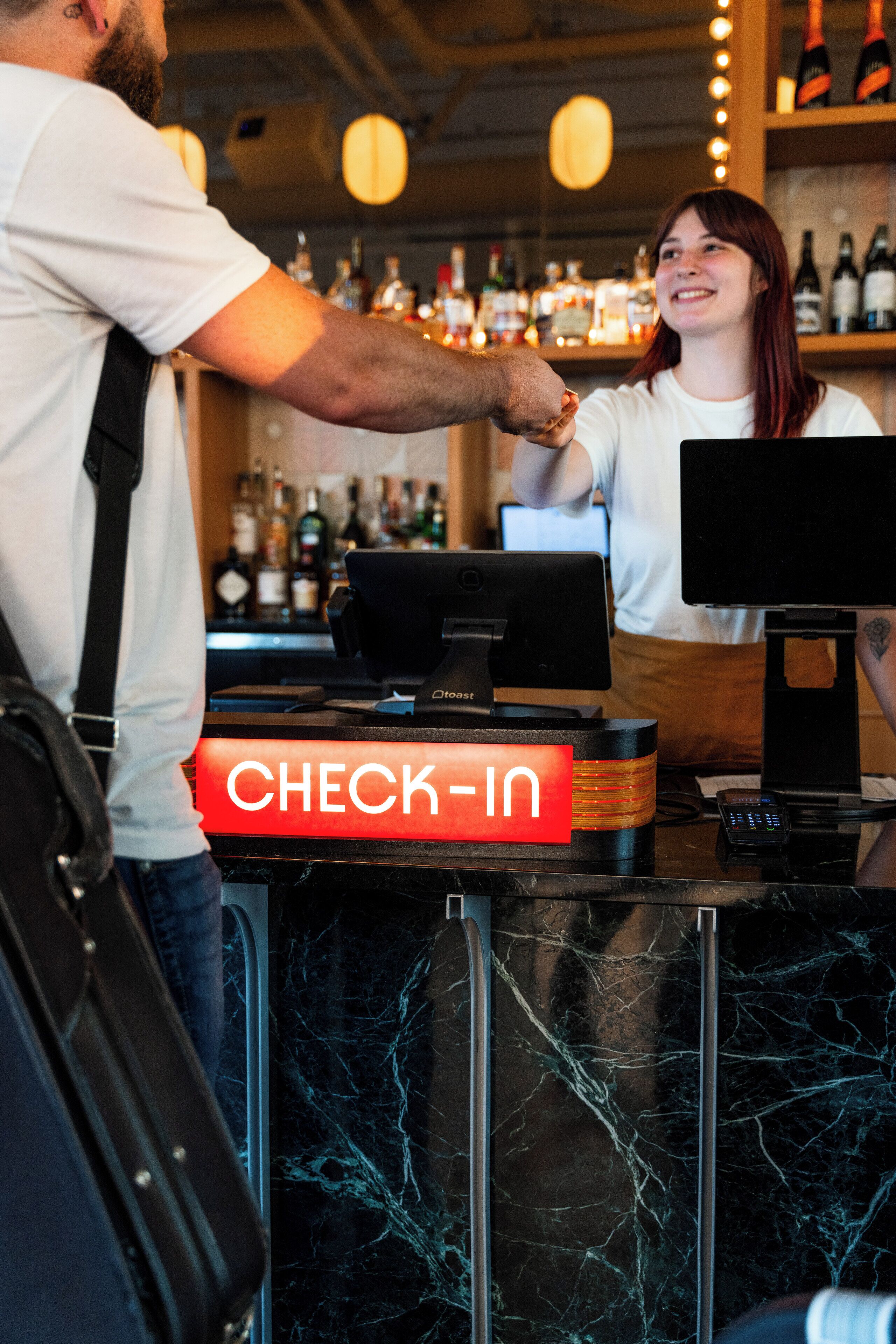 En bar med en receptionsdisk, en computerskærm og diverse flasker i baggrunden.
