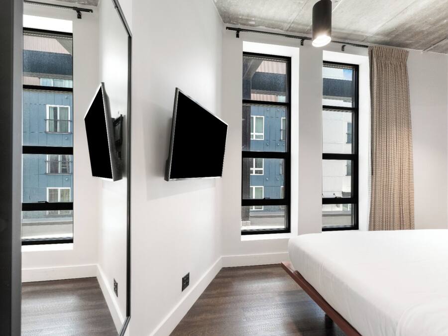 Ein modernes Hotelzimmer mit einem großen Bett, zwei Fenstern und einem an der Wand befestigten Flachbildfernseher.