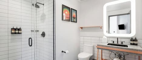 A modern bathroom with a glass-enclosed shower, a toilet, a sink with a mirror, and a towel rack.