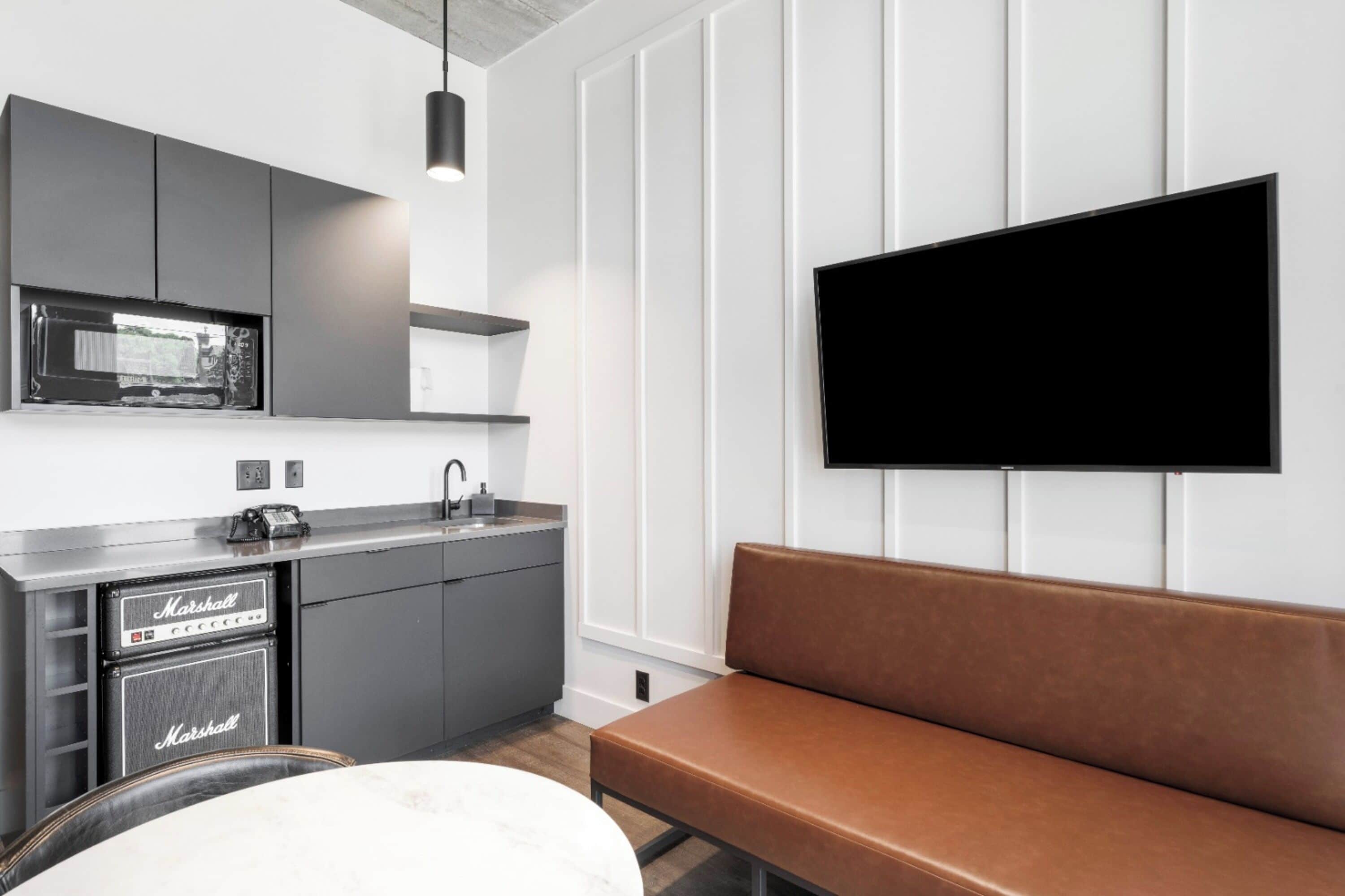 Una cucina moderna con mobili grigi, un piano di lavoro nero, un amplificatore Marshall e una panca marrone.