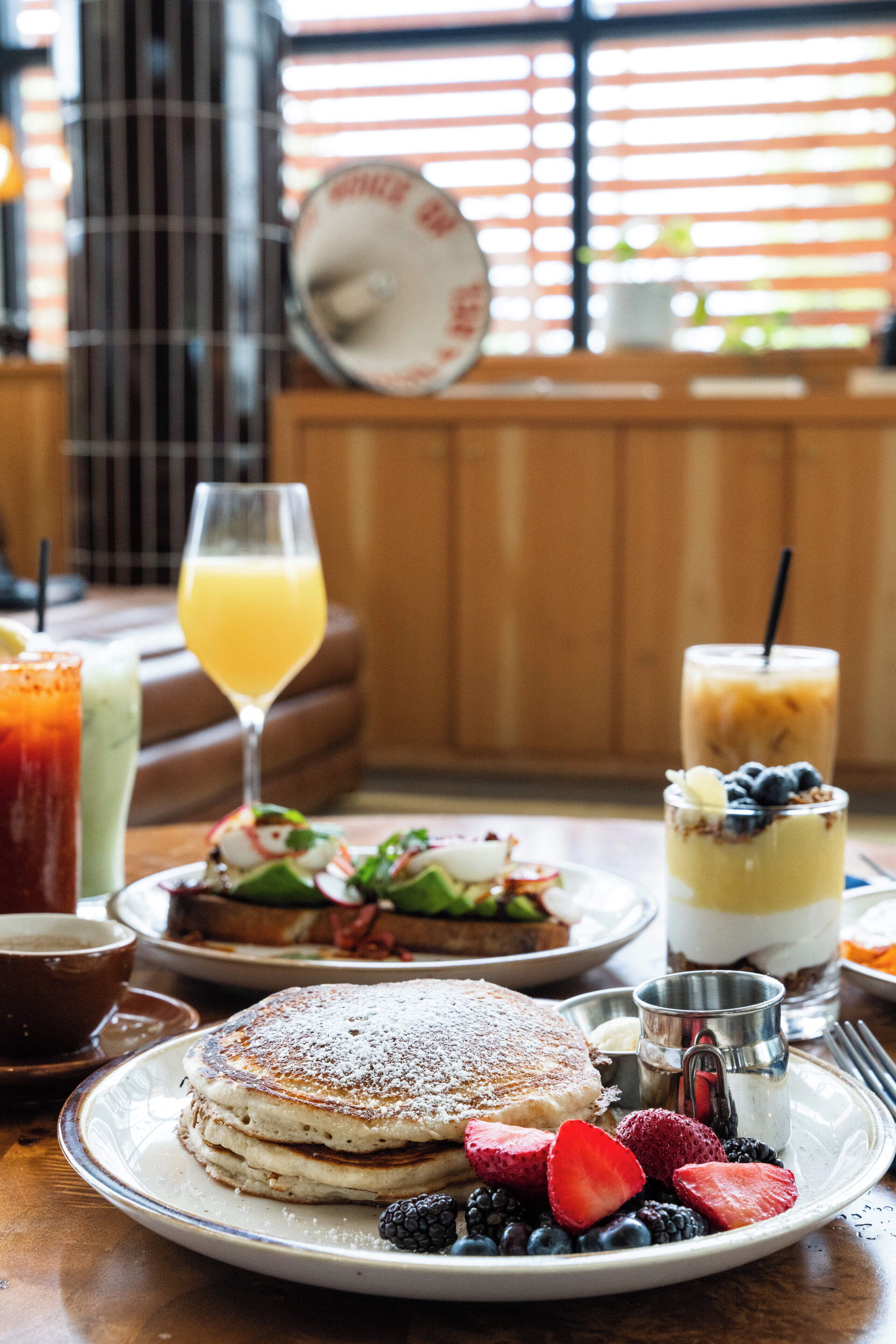 A breakfast setting with pancakes, fresh berries, and various beverages on a wooden table.