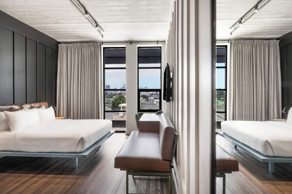 A modern hotel room with two beds, a sofa, and large windows offering a city view.