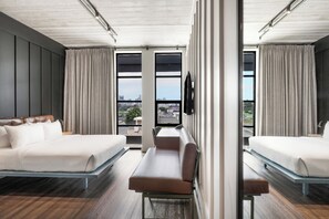 Une chambre d’hôtel moderne avec deux lits, un canapé et de grandes fenêtres donnant sur la ville.