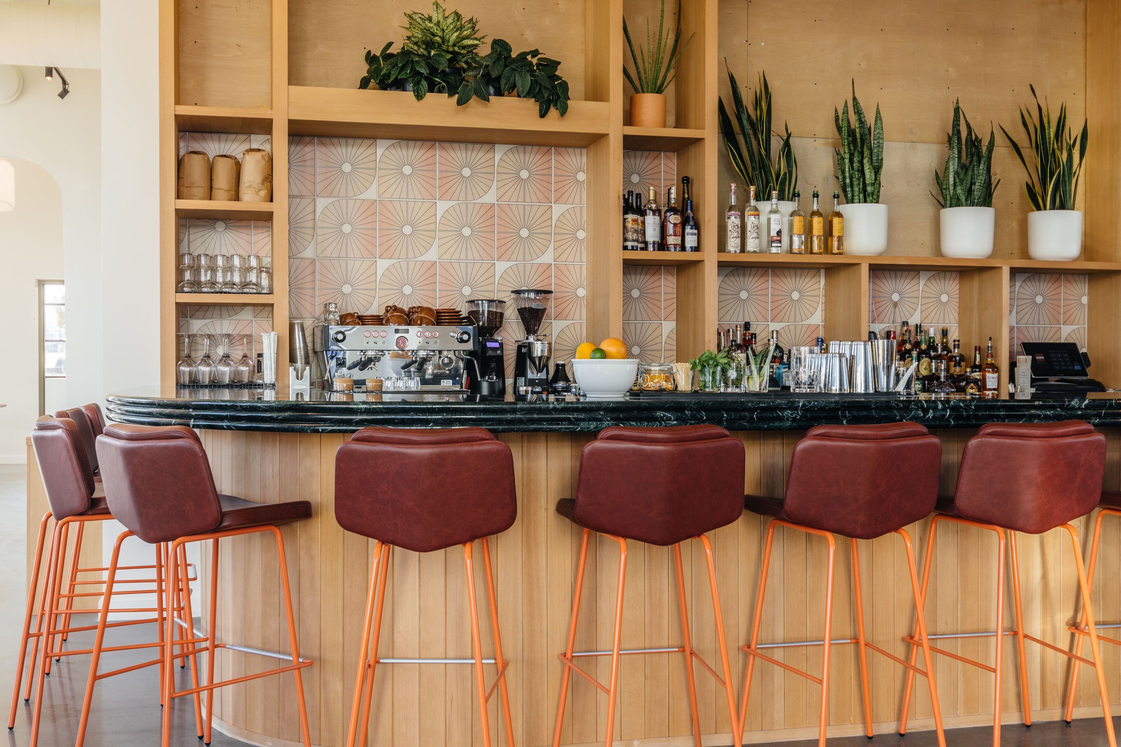 A bar area with wooden shelves, bar stools, and a coffee machine.