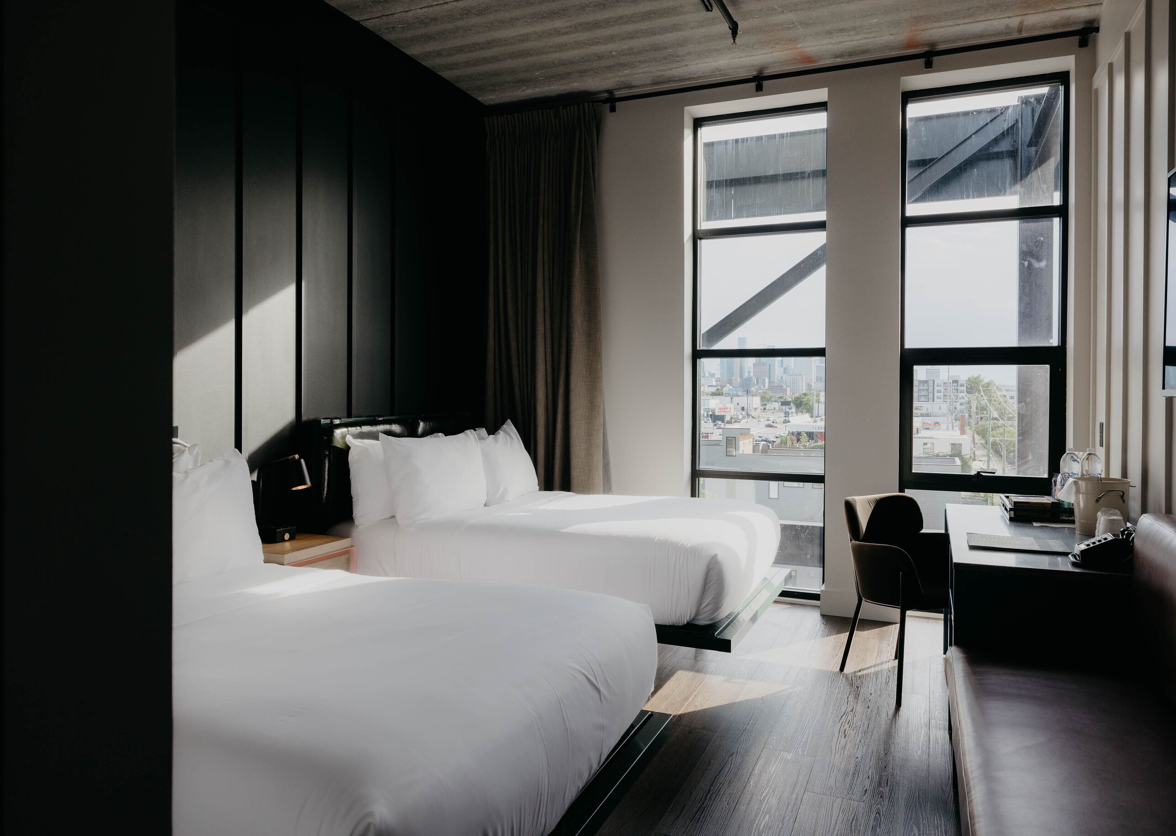 Une chambre d’hôtel avec deux lits, un bureau et une vue sur le paysage urbain, grâce à de grandes fenêtres.