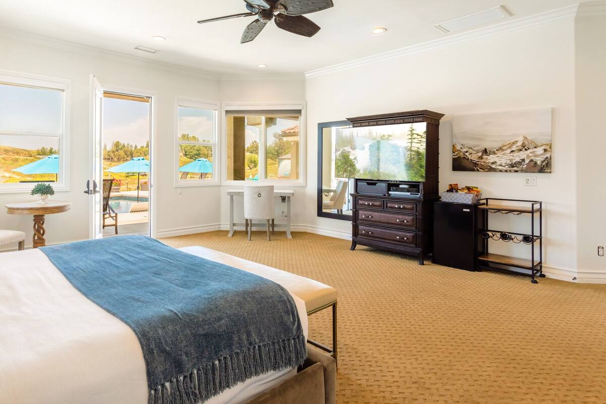 A spacious bedroom with a large bed, a desk, and a television.