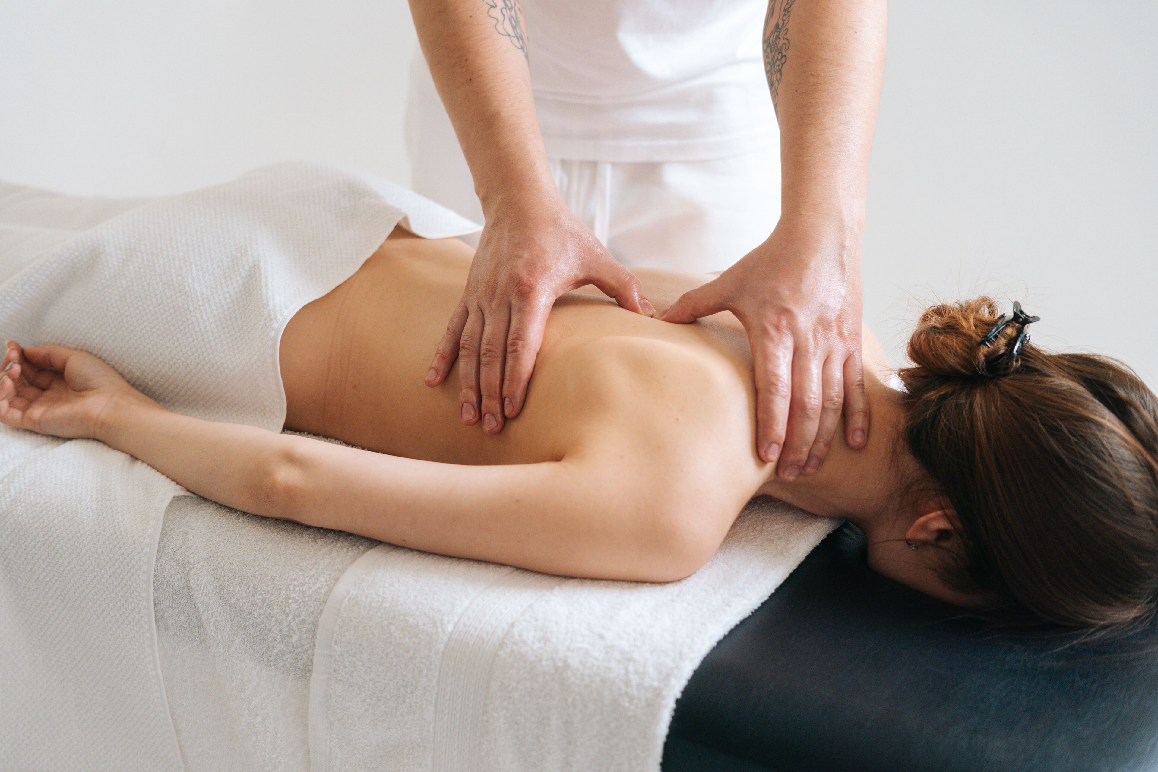 A person receiving a back massage on a massage table in a room with a plain white wall and a simple, uncluttered design.