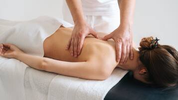 A person receiving a back massage on a massage table in a room with a plain white wall and a simple, uncluttered design.