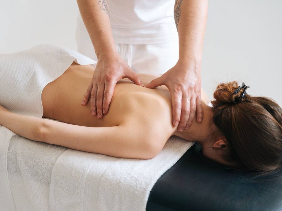 A person receiving a back massage on a massage table in a room with a plain white wall and a simple, uncluttered design.