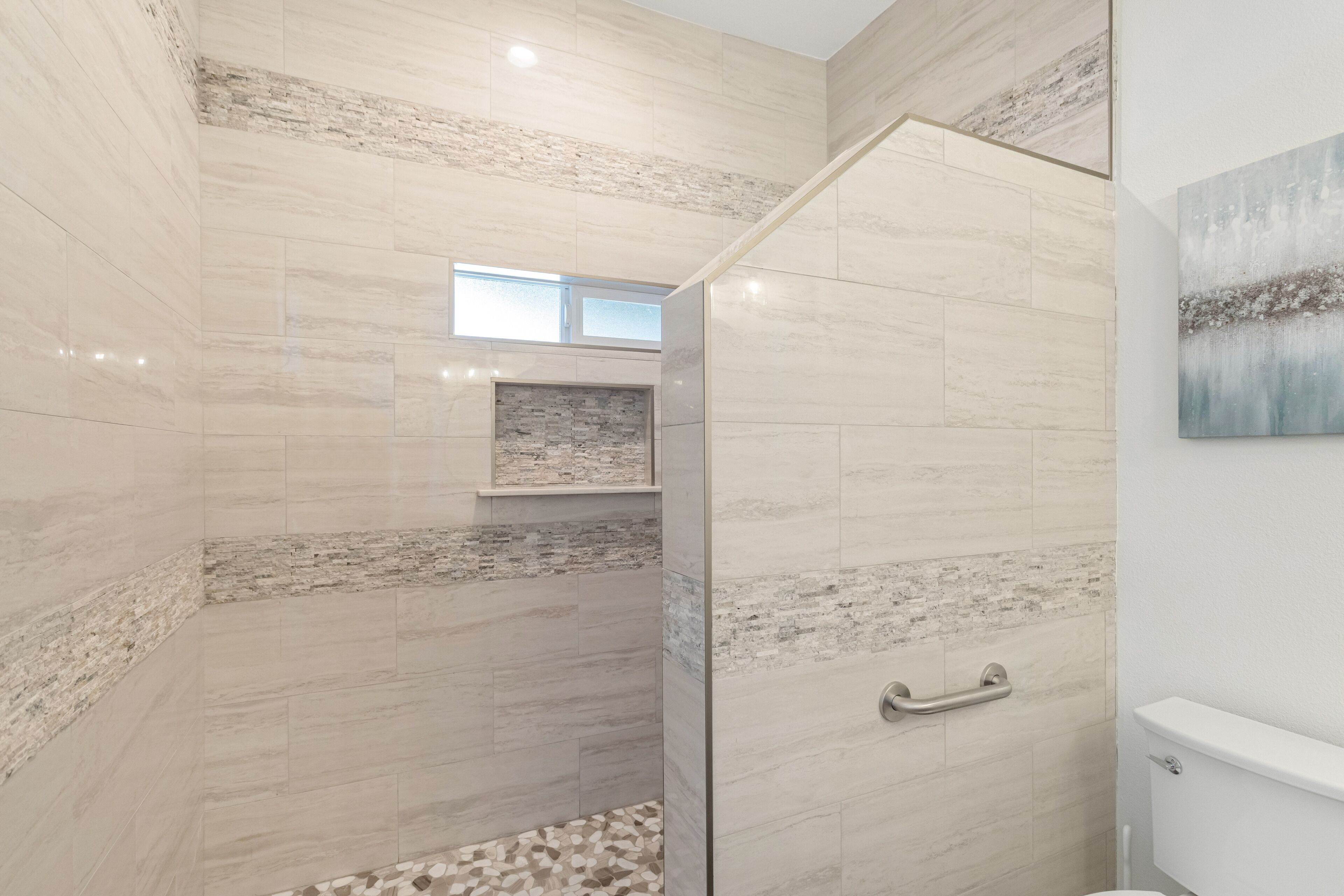 A modern bathroom with a shower area, a toilet, and a small shelf with a decorative item.