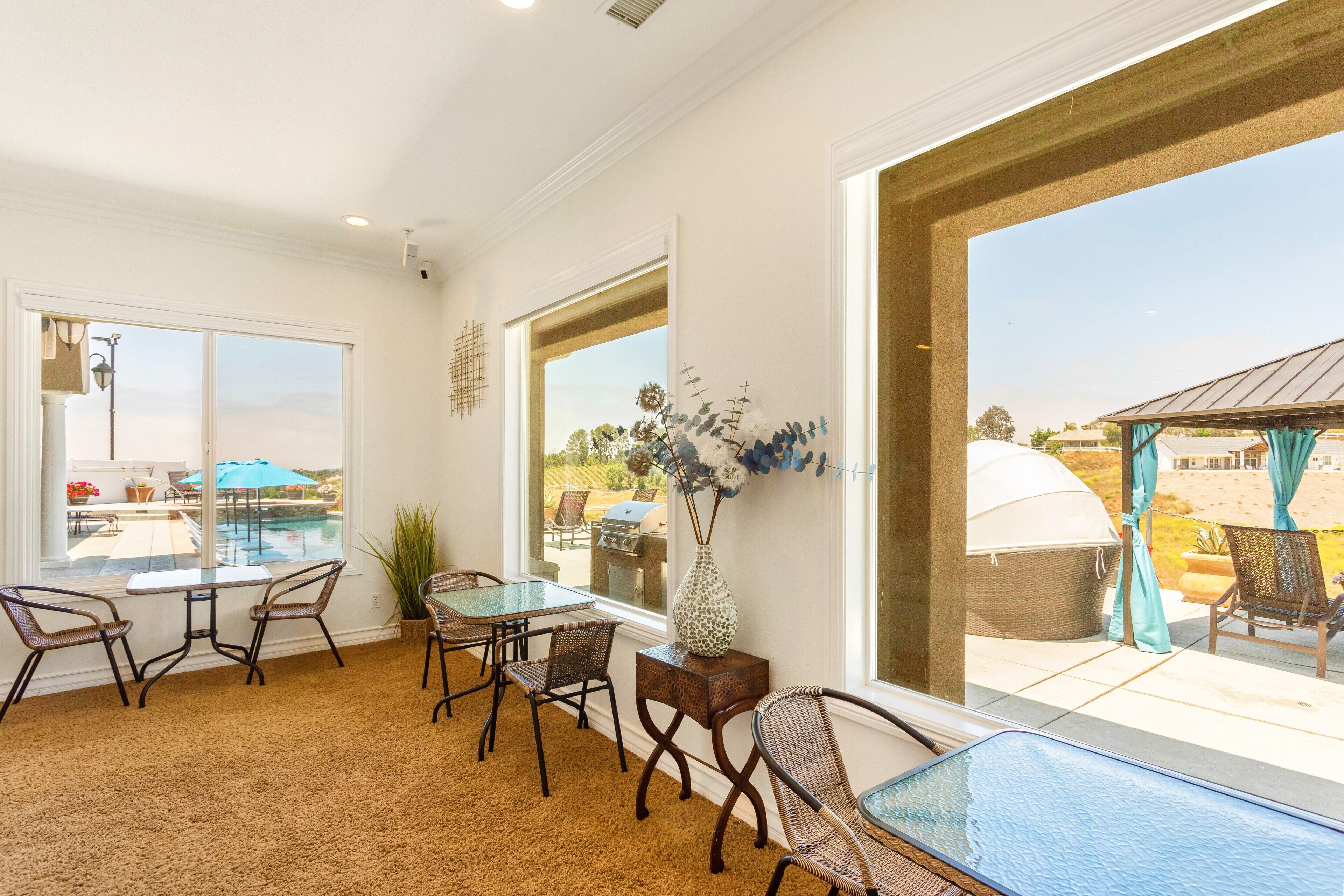 A spacious room with a large window, a glass table, wicker chairs, and a decorative vase.