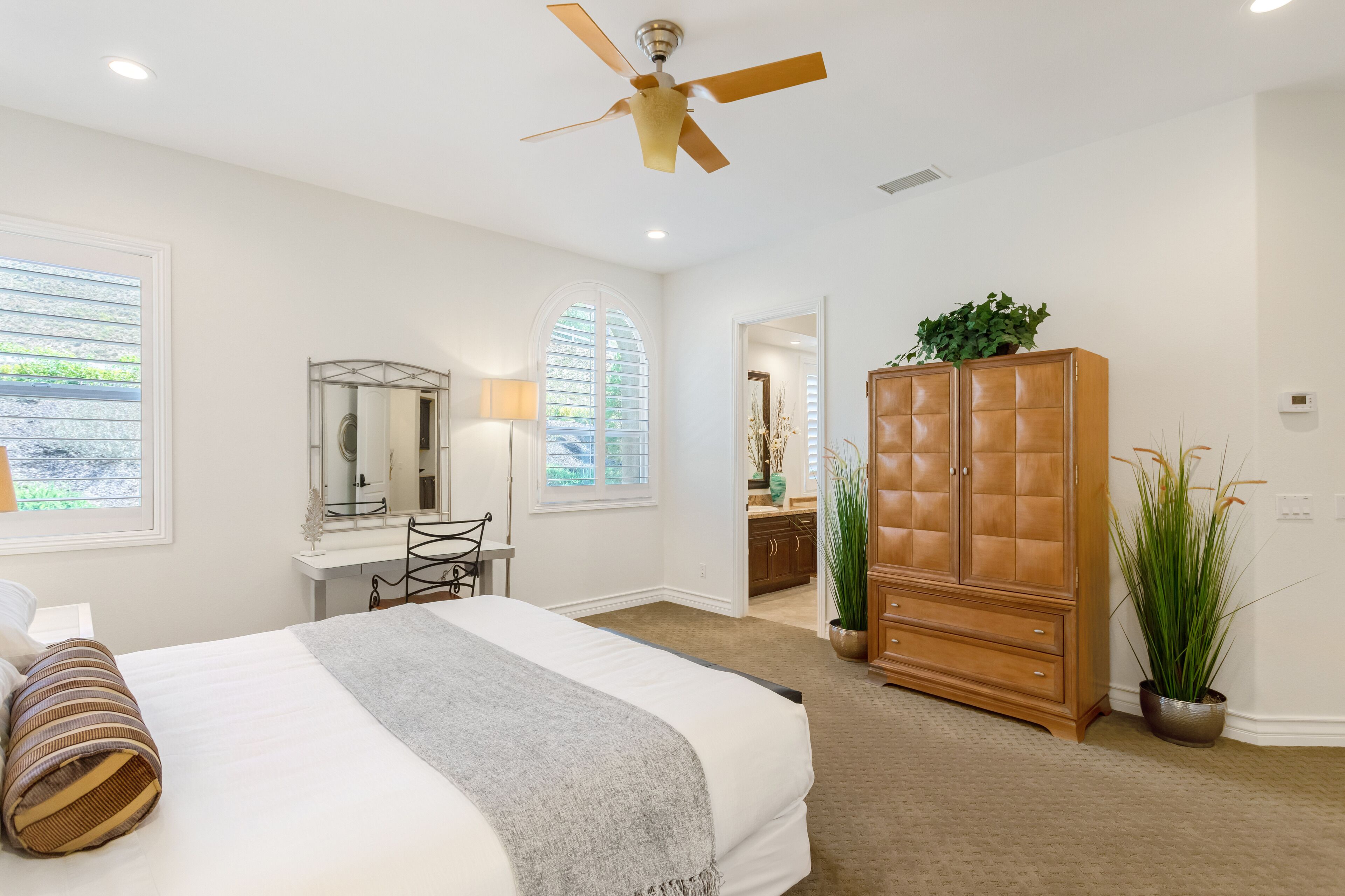 A bedroom with a bed, a desk, a wardrobe, and a ceiling fan.