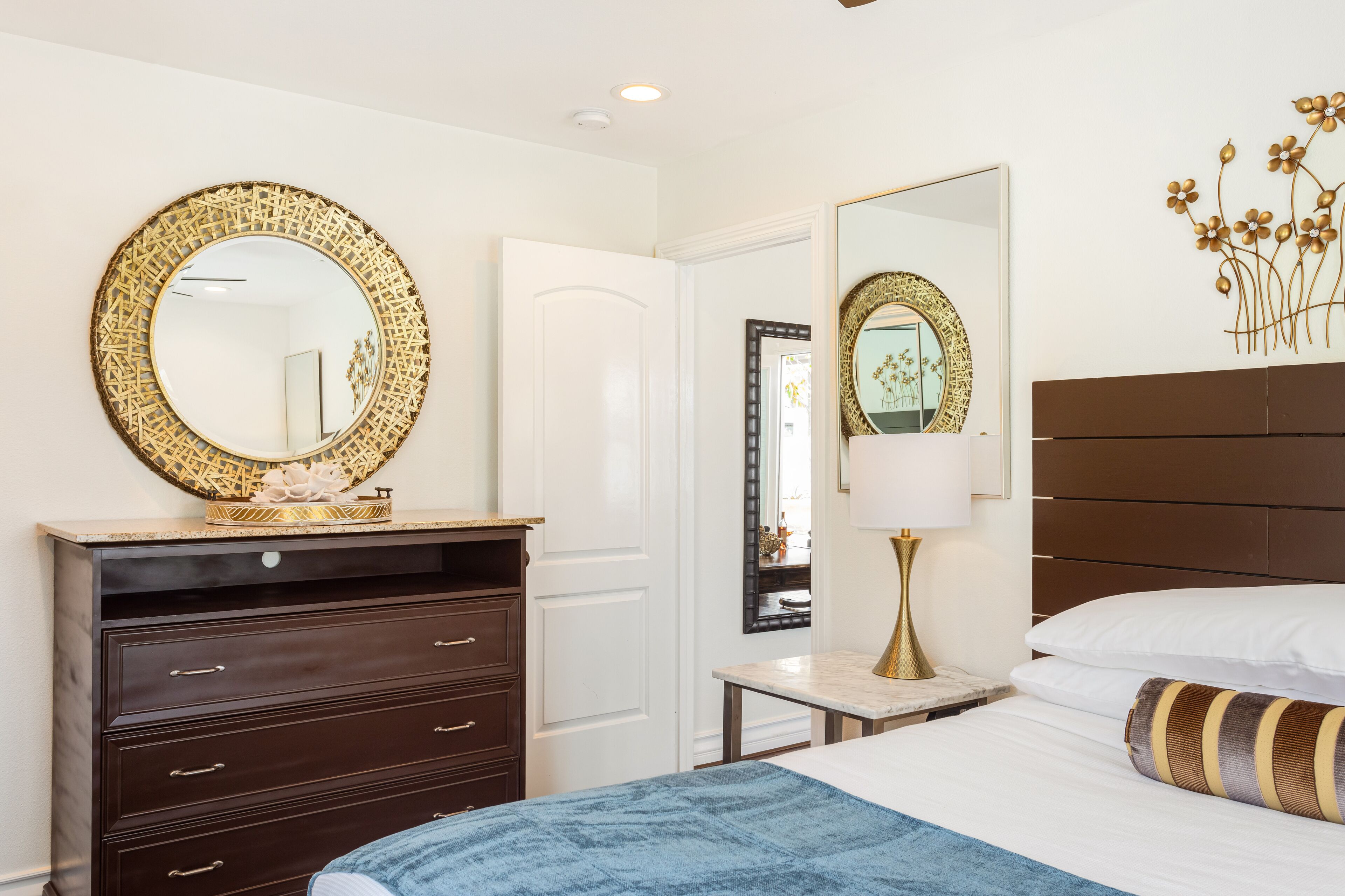 A hotel room with a bed, a dresser, a mirror, a nightstand, and a wall-mounted decorative piece.