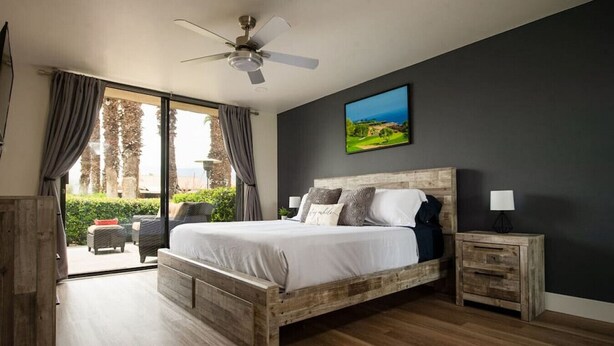 Une chambre à coucher avec un lit en bois, un ventilateur de plafond, une table de chevet et une vue sur l’extérieur.