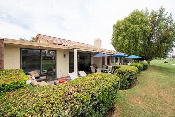 A modern house with a covered patio, outdoor seating, and a well-maintained lawn.