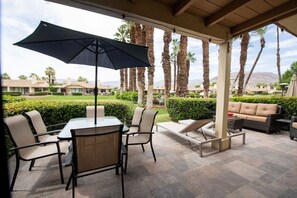 A covered outdoor patio with a table and chairs, a sofa, and an umbrella.