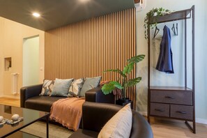 Un salon moderne avec un canapé, une table basse et une plante. On y trouve un porte-manteau avec une veste et un radiateur fixé au mur.