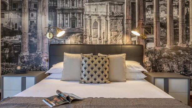 A bedroom with a large bed, two nightstands, and a wall mural of ancient ruins. - Oscar Garden Appartment   close to S. Pietro (ROMA)
