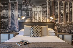 A bedroom with a large bed, two nightstands, and a wall mural of ancient ruins.