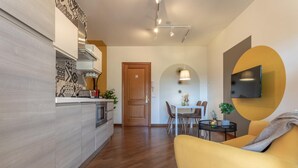 A modern kitchen with a built-in oven and microwave, a dining area with a table and chairs, and a living area with a sofa and a TV mounted on the wall. - Oscar Garden Appartment   close to S. Pietro (ROMA)