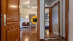 A hotel room with a wooden door, a dining area with a table and chairs, a TV mounted on the wall, and a bed with a cityscape view. - Oscar Garden Appartment   close to S. Pietro (ROMA)