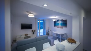 A modern living room with a sofa, dining table, and a TV mounted on the wall.