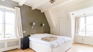 Une chambre à coucher avec un lit blanc, un radiateur, deux lampes fixées au mur et une fenêtre avec des rideaux.