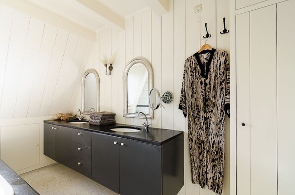 A bathroom with a black vanity, two mirrors, a sink, and a robe hanging on a door.