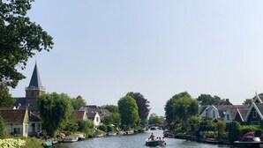 Un canal bordé de bateaux, de maisons et d’un clocher d’église.
