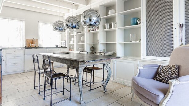 Une cuisine avec une table à manger, des chaises et des luminaires suspendus.
