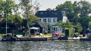 Une maison avec une jetée qui s’avance sur une étendue d’eau calme, entourée d’une végétation luxuriante.