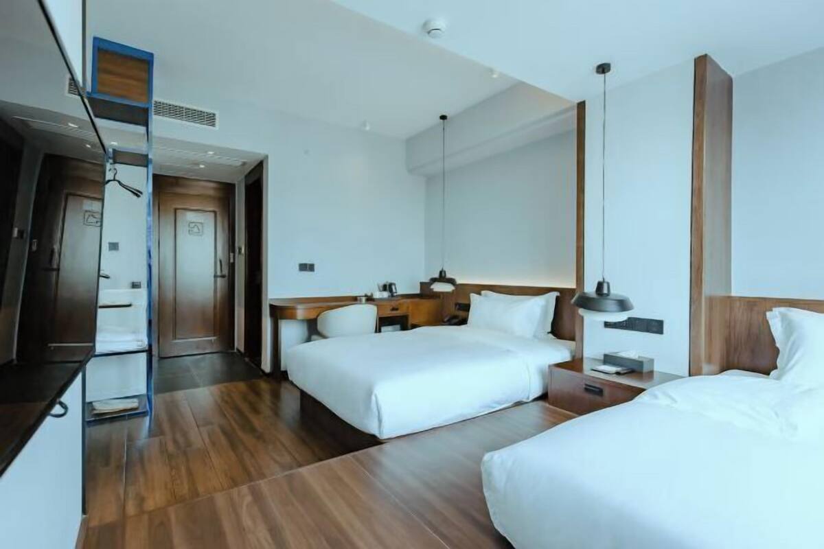 A hotel room with two beds, a desk, a chair, a lamp, and a mirror.