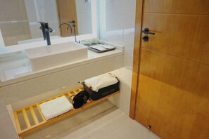 A modern bathroom with a large white sink, a mirror, and a wooden shelf with a towel and a bag. - Guang Ao Hotel (Haikou)