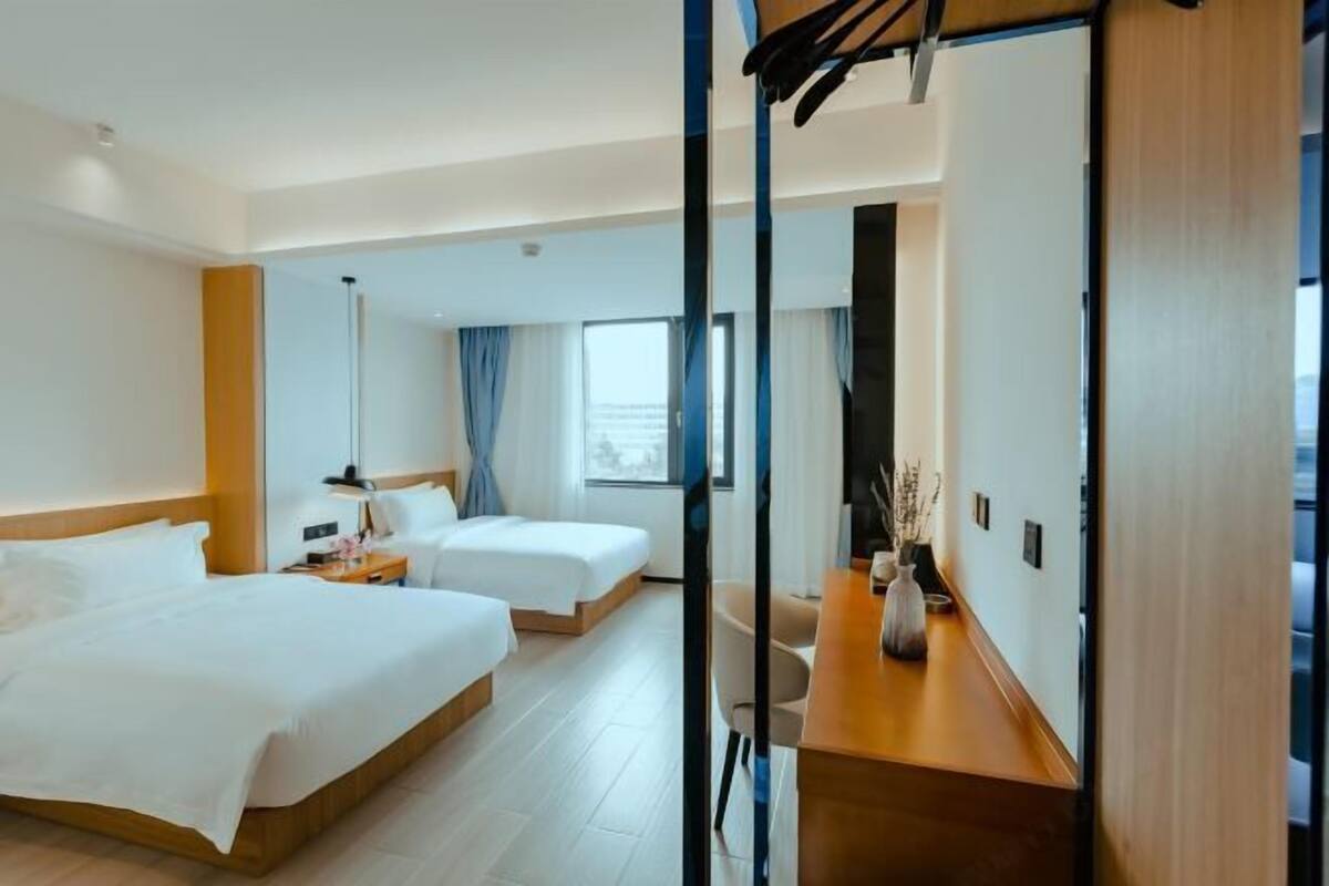 A modern hotel room with two beds, a wooden desk, and a large mirror.