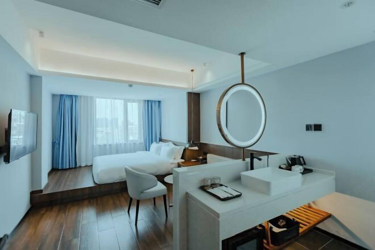 A modern hotel room with a bed, a desk with a mirror, a sink, and a TV.