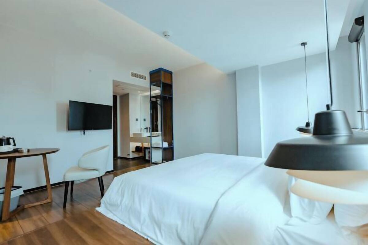A modern hotel room with a bed, a desk, a chair, a TV, and a mirror.