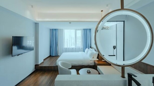 Una habitación de hotel moderna con una cama, un televisor, un espejo redondo y una zona de estar.