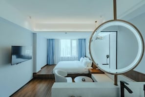 A modern hotel room with a bed, a TV, a round mirror, and a seating area. - Guang Ao Hotel (Haikou)
