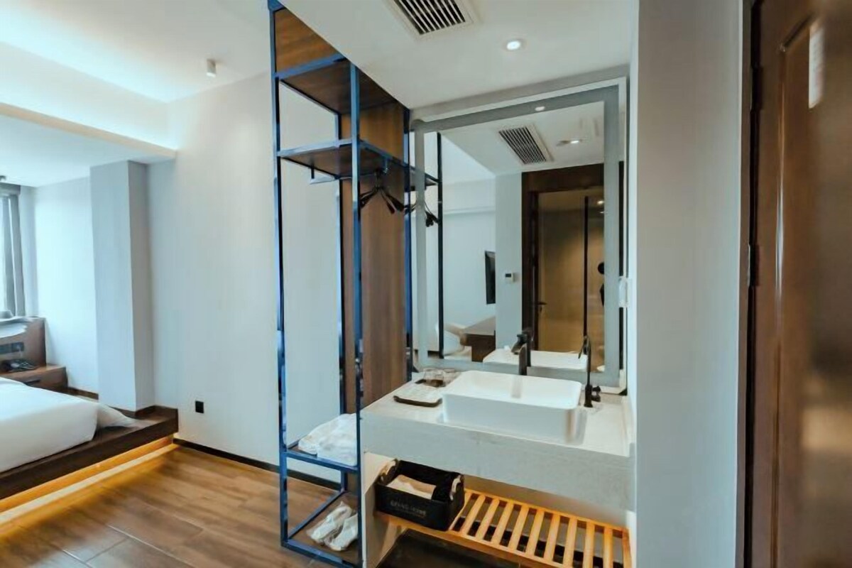 A modern hotel room with a large bed, a built-in wardrobe, a large mirror, and a white sink.