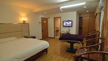 A hotel room with a bed, bedside table, TV, and wooden chairs.