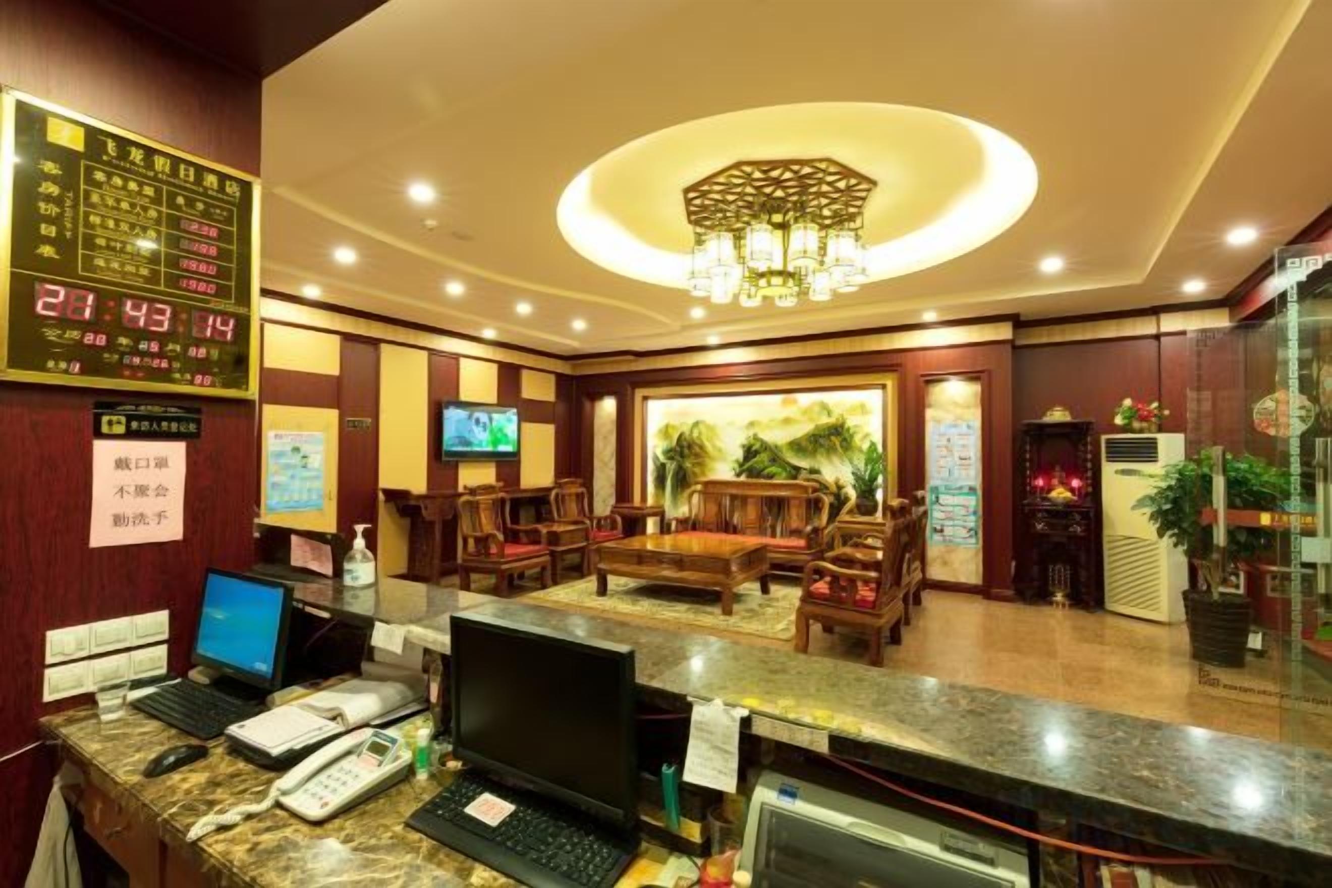Zona de recepción de hotel con pantalla digital, asientos, televisor y candelabro.