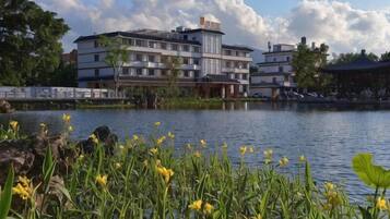 A building with multiple floors, a body of water in the foreground, and greenery around.