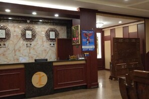Zona de recepción de un hotel con mostrador de mármol, relojes y un escritorio de madera.