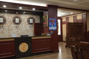 Zona de recepción de un hotel con mostrador de mármol, relojes y un escritorio de madera.