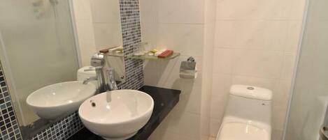 A bathroom with two sinks, a toilet, and a glass shelf with toiletries.