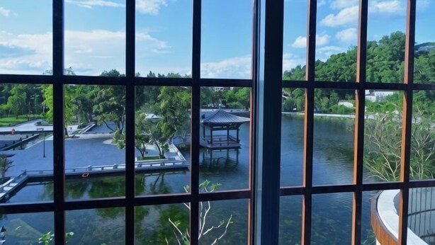 A view through a window with a grid pattern, a body of water, and a structure with a roof. - Feilong Holiday Hotel (Xinxing)
