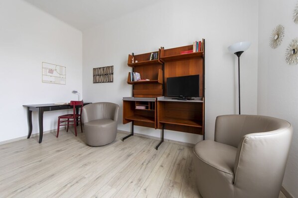 Ein modernes Wohnzimmer mit einem Holz-TV-Schrank, einem Schreibtisch, zwei Stühlen und einer Stehlampe.