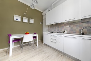 A modern kitchen with white cabinets, a tiled backsplash, and a dining area with a white table and purple chairs.