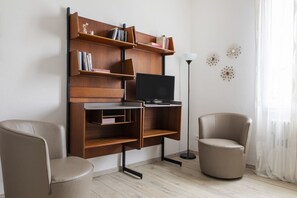 A modern living room with a wooden entertainment unit, a flat-screen TV, two leather armchairs, and a floor lamp.