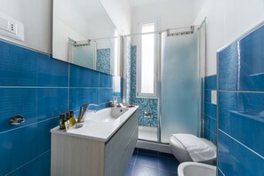 A bathroom with blue tiles, a white sink, a shower, and a toilet. - UR-NEST Mitelli, a bedroom (Bologna)